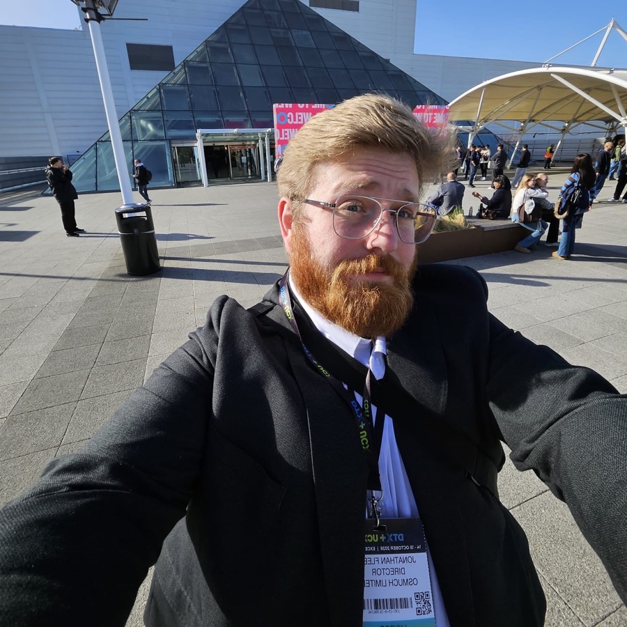 Jonathan Fleet taking a selfie outside the glass pyramid entrance of ExCeL London, wearing his DTX + UCX badge